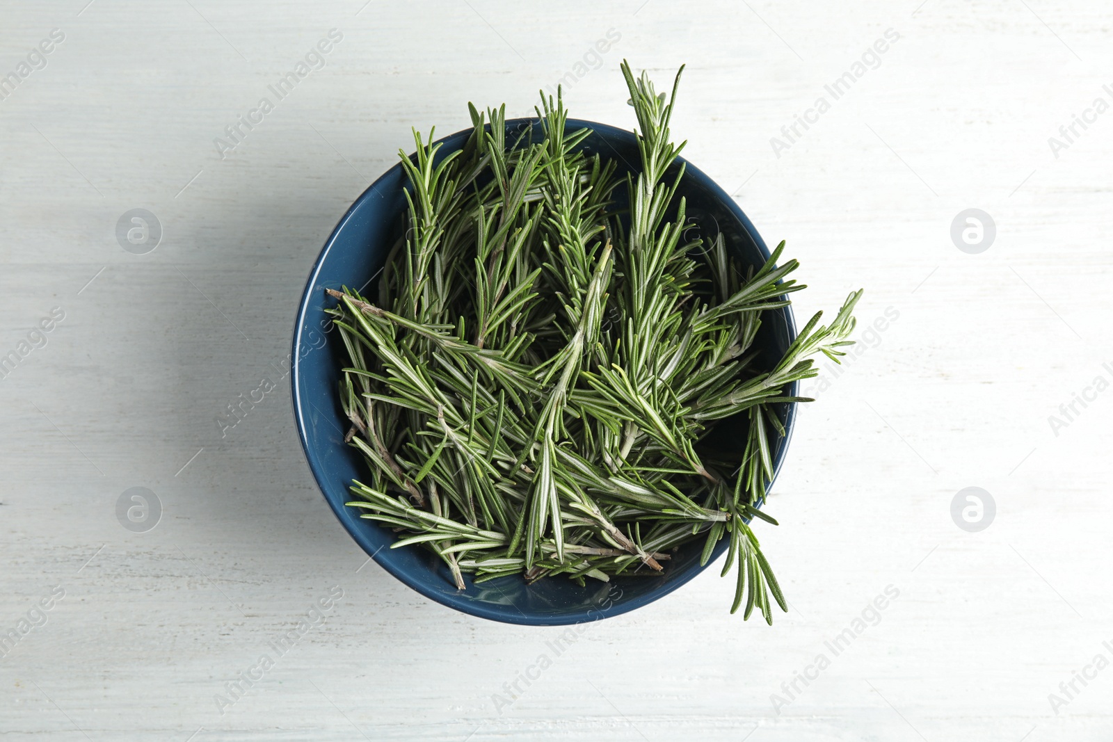 Photo of Bowl with fresh rosemary twigs on wooden table, top view