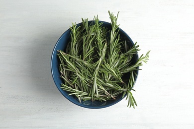 Bowl with fresh rosemary twigs on wooden table, top view