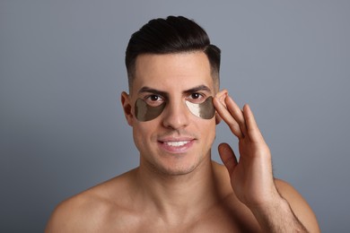 Photo of Man applying dark under eye patch on grey background