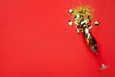 Flat lay composition with confetti and champagne glass on red background. Space for text