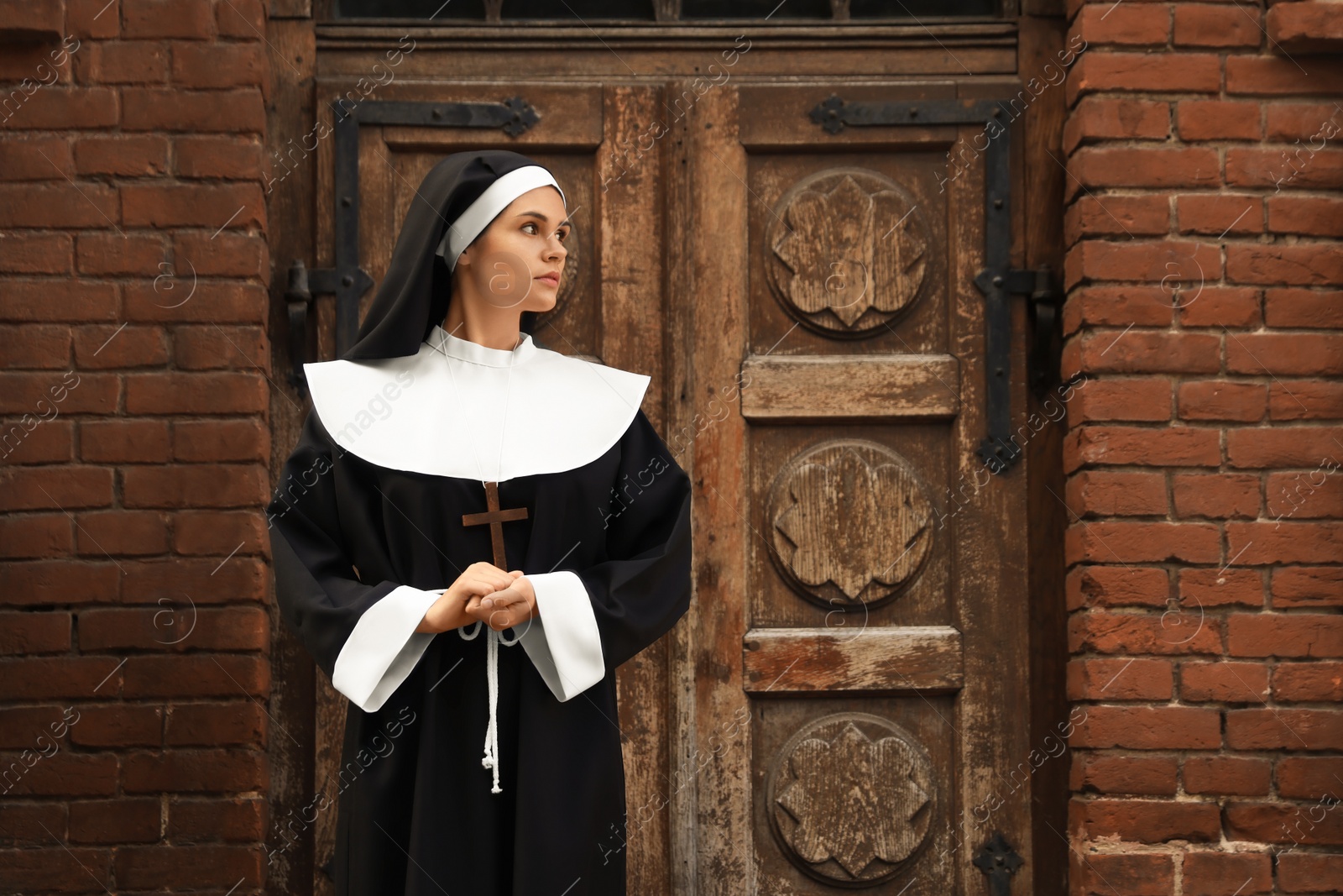 Photo of Young nun with Christian cross near old building outdoors