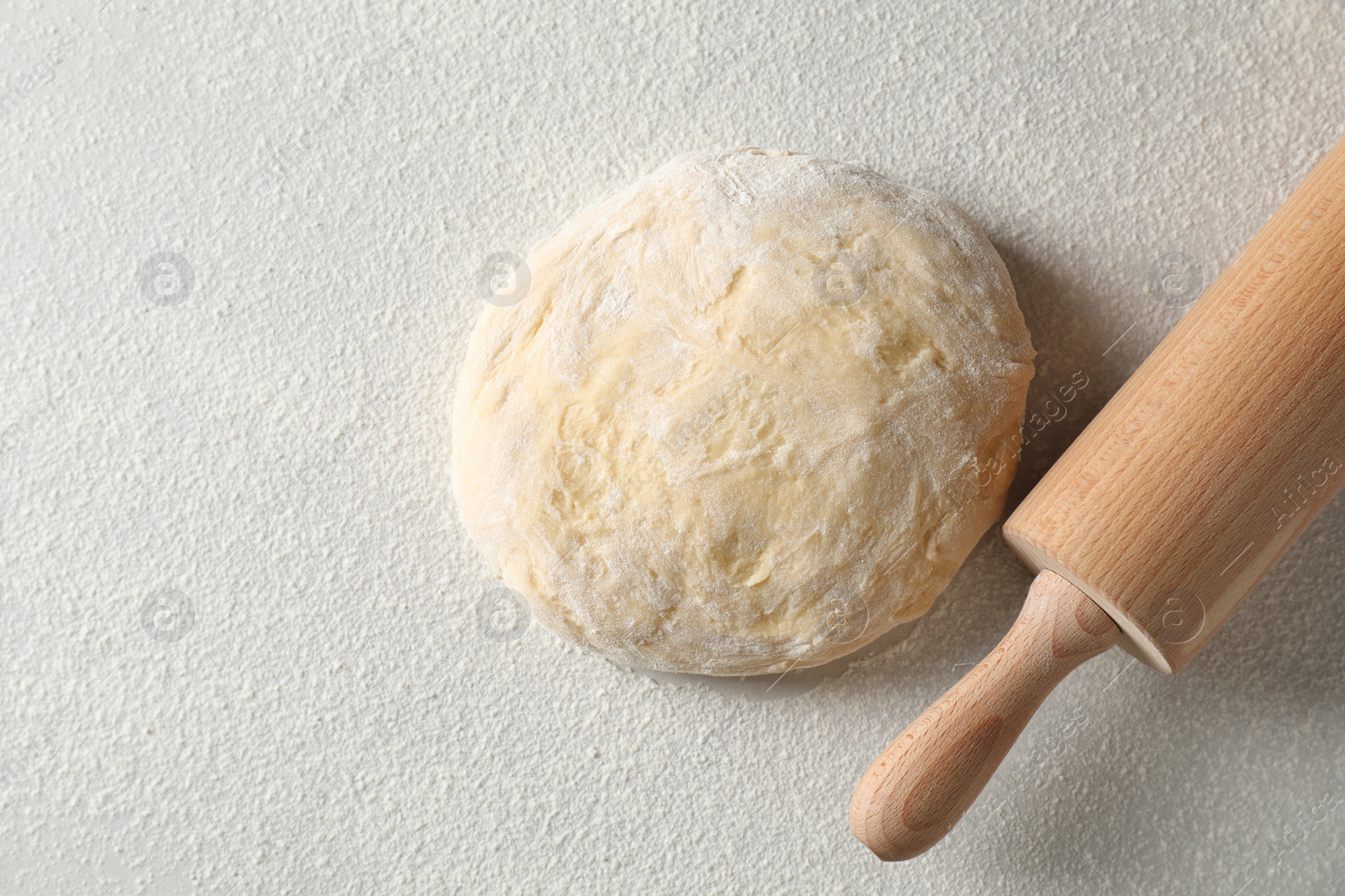 Photo of Raw dough and rolling pin on white table, top view. Space for text