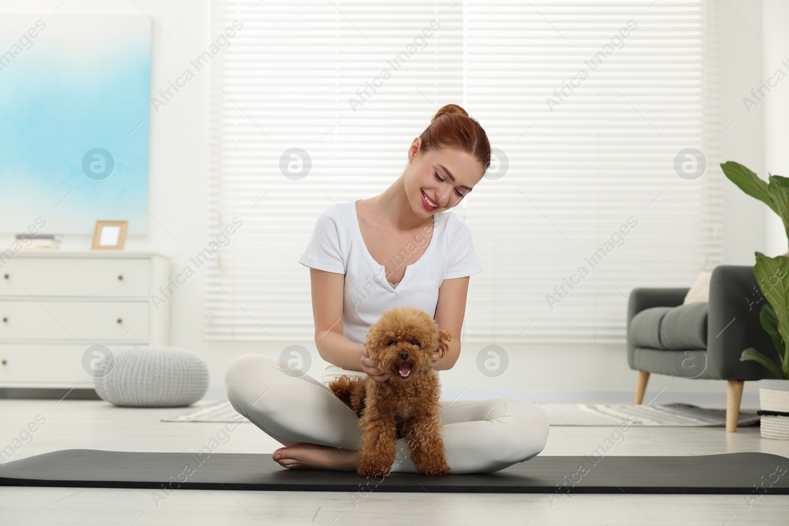 Photo of Happy young woman practicing yoga on mat with her cute dog at home