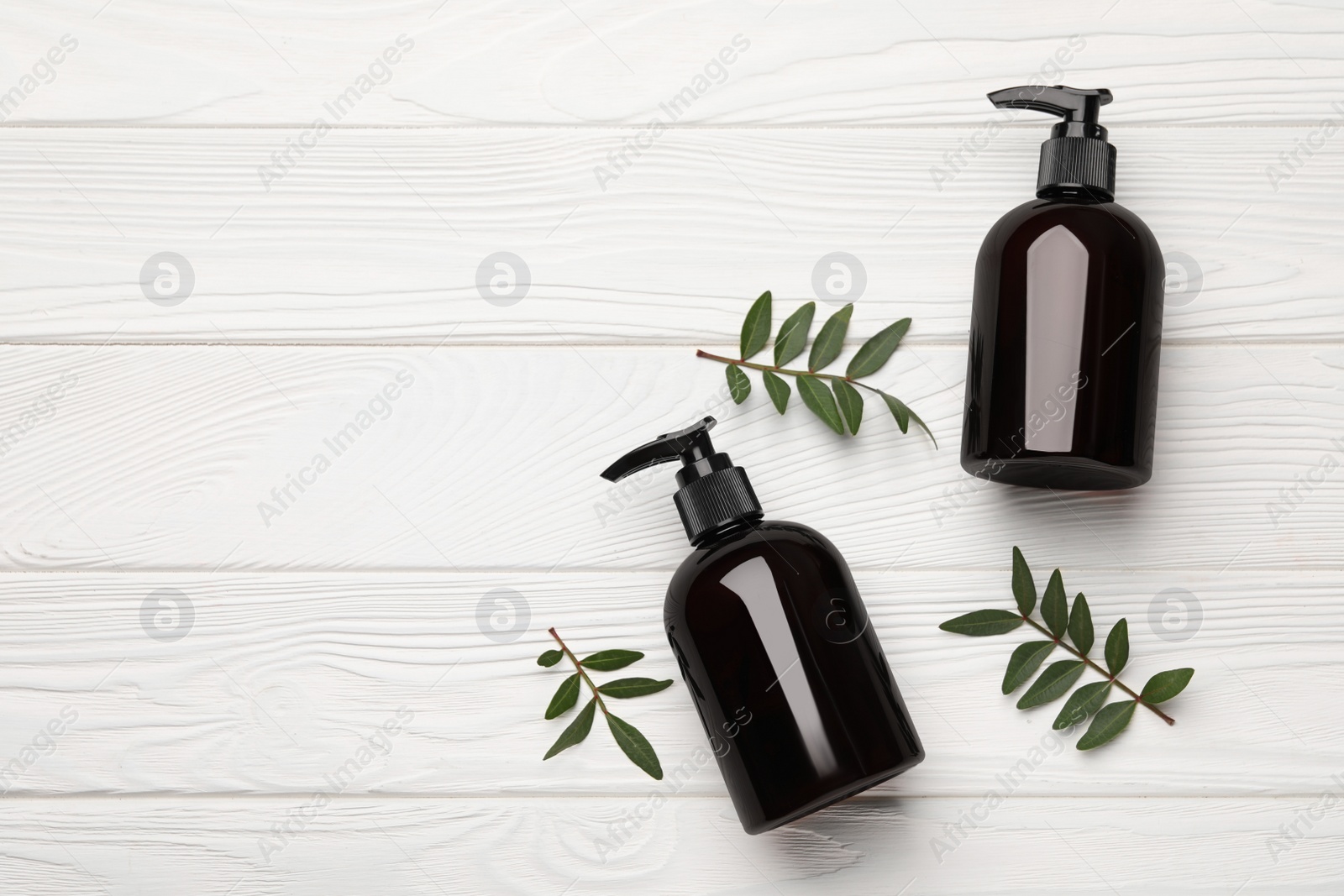 Photo of Shampoo bottles and green leaves on white wooden table, flat lay. Space for text