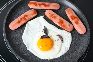 Photo of Egg and sausages in frying pan on stove, closeup