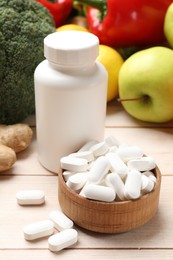 Photo of Dietary supplements. Bottle and bowl with pills near food products on light wooden table, closeup