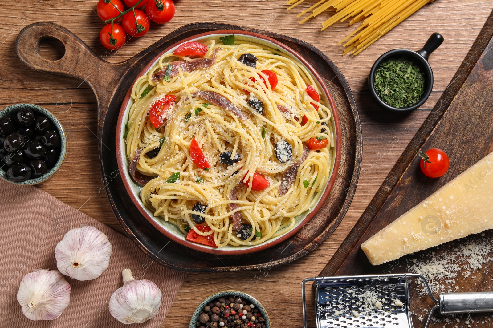 Photo of Plate of delicious pasta with anchovies and ingredients on wooden table, flat lay