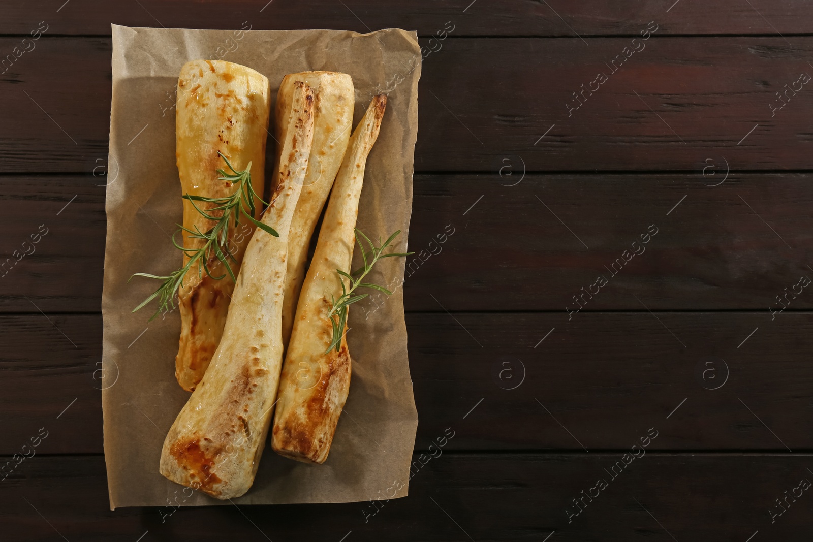 Photo of Tasty baked parsnips and rosemary on wooden table, top view. Space for text