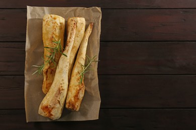 Photo of Tasty baked parsnips and rosemary on wooden table, top view. Space for text