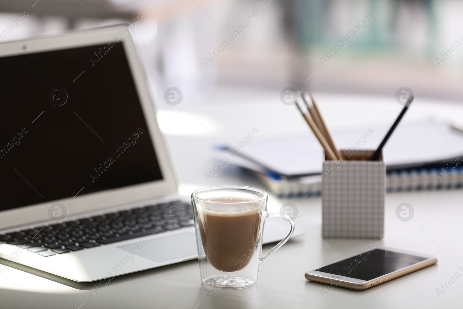 Photo of Cup of coffee, mobile phone and laptop on table