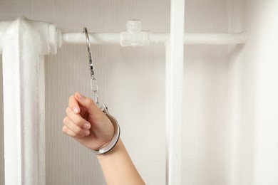 Photo of Woman handcuffed to radiator near white wall indoors, closeup