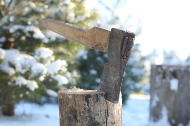 Metal axe in wooden log outdoors on sunny winter day, closeup