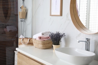 Bathroom counter with vessel sink, flowers and towels in bathroom interior. Idea for design