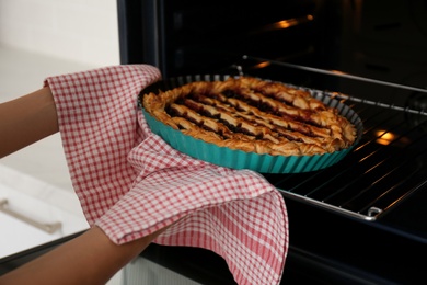 Photo of Woman taking delicious fresh homemade cake out of oven indoors, closeup