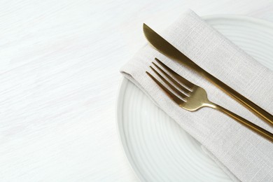 Stylish ceramic plate, cutlery and napkin on white wooden table, above view. Space for text