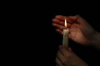 Photo of Woman holding burning candle in hands on black background, closeup. Space for text