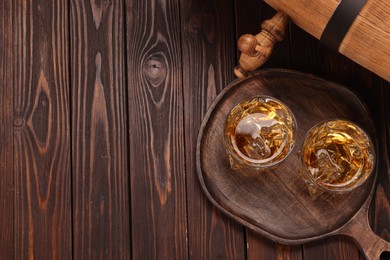 Photo of Whiskey with ice cubes in glasses and barrel on wooden table, top view. Space for text