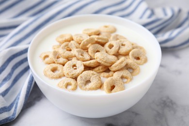 Photo of Breakfast cereal. Tasty corn rings with milk in bowl on white marble table, closeup