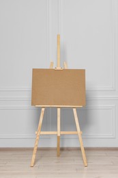 Wooden easel with blank board near white wall indoors