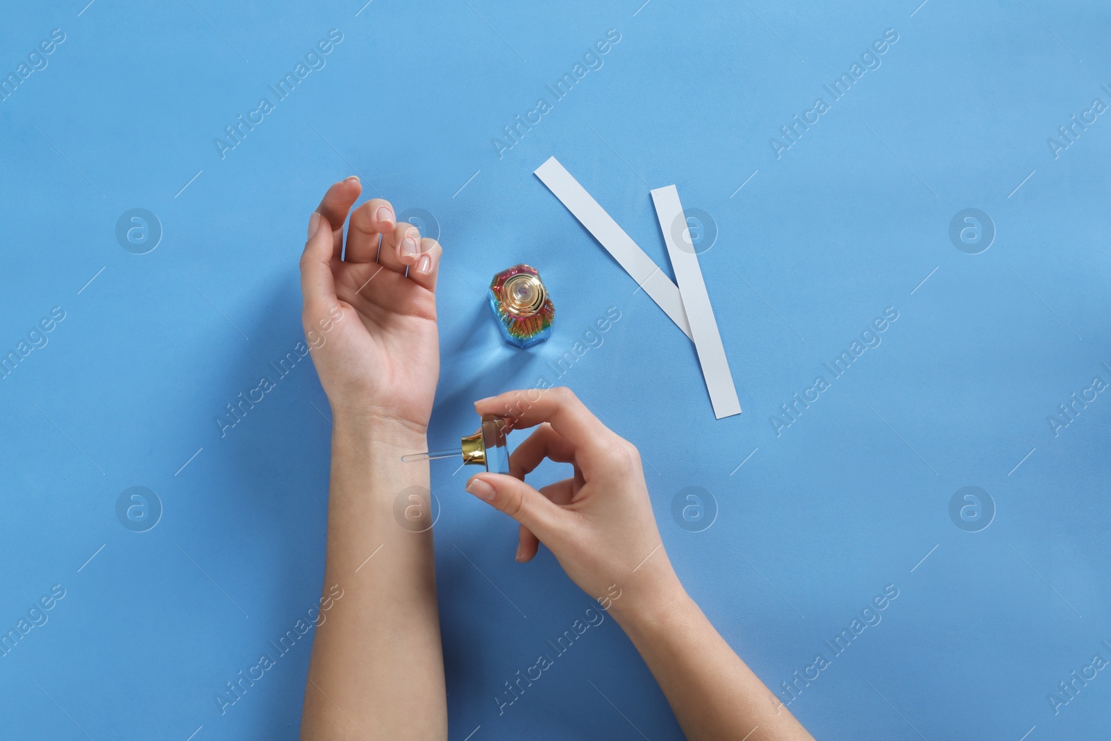 Photo of Woman applying perfume on blue background, top view