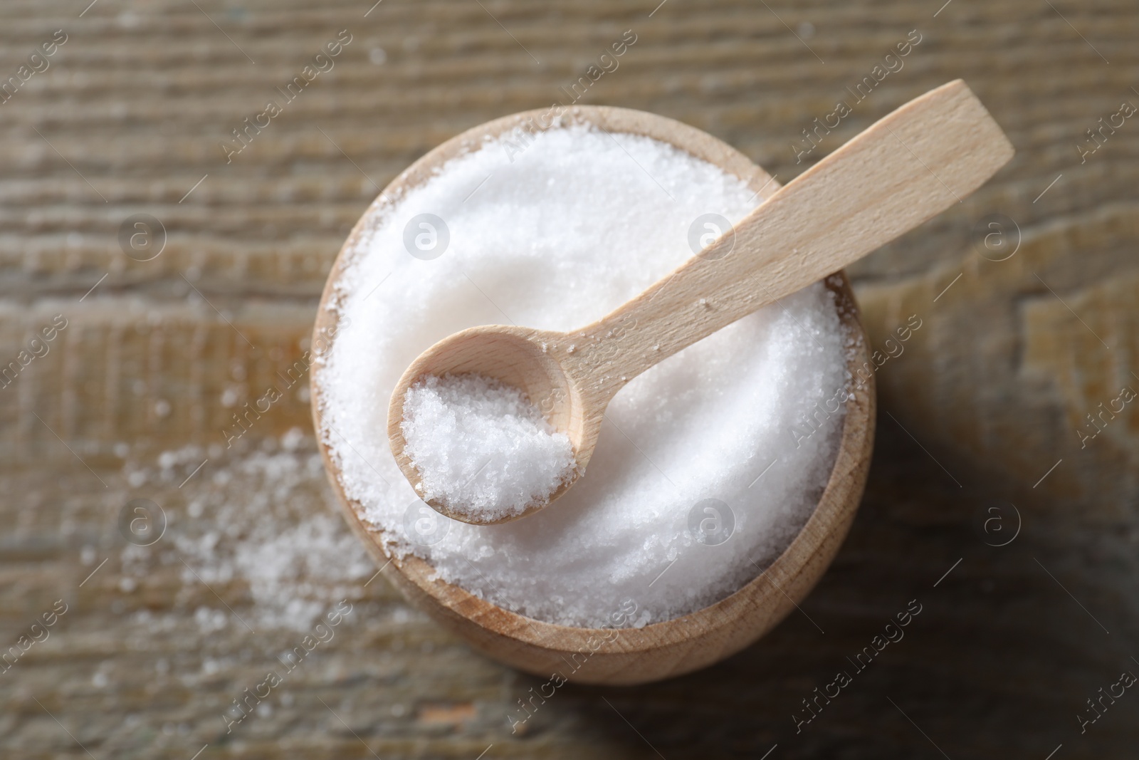 Photo of Organic salt in bowl and spoon on wooden table, top view