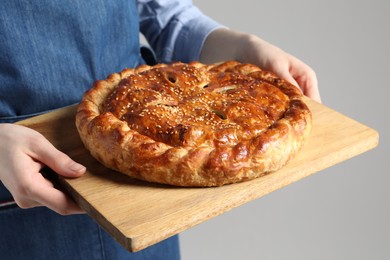 Photo of Woman holding tasty homemade pie on light grey background, closeup