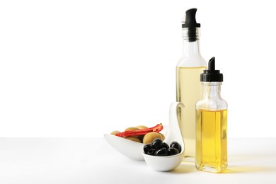 Photo of Bottles of different cooking oils and olives on white background