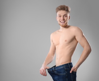Photo of Young man with slim body in old big size jeans on grey background. Space for text