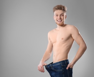 Young man with slim body in old big size jeans on grey background. Space for text