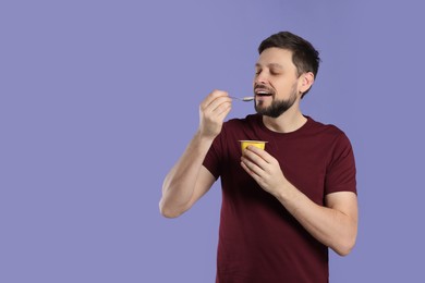 Photo of Handsome man eating tasty yogurt on purple background. Space for text
