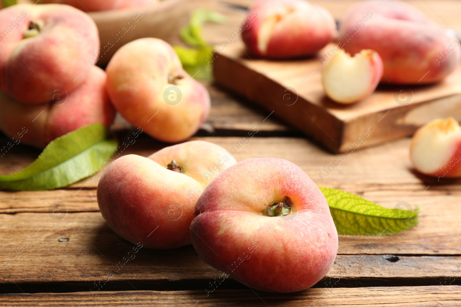 Photo of Fresh ripe donut peaches with leaves on wooden table, closeup