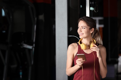 Photo of Young woman with headphones and mobile device at gym