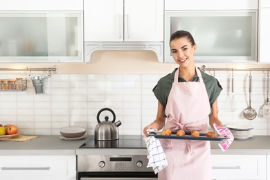 Photo of Young woman holding oven sheet with croissants in kitchen, space for text