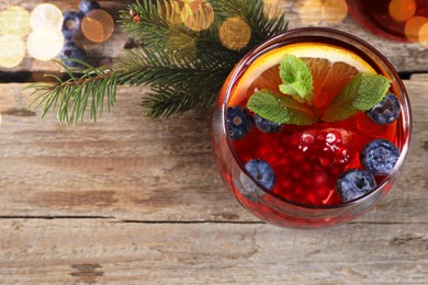 Photo of Aromatic Christmas Sangria drink in glass and fir branches on wooden table, flat lay. Space for text
