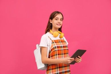 Photo of Teenage student with backpack, headphones and tablet on pink background