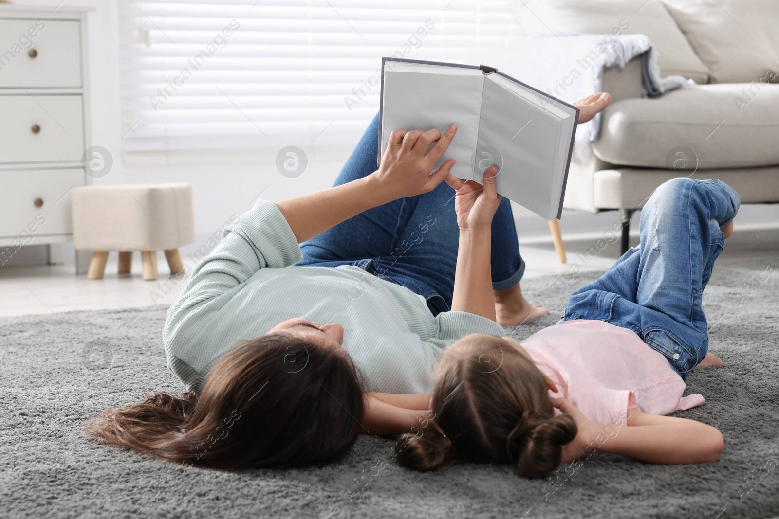 Photo of Young mother and her daughter reading book on floor at home