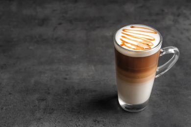 Photo of Glass cup with delicious caramel latte on grey background