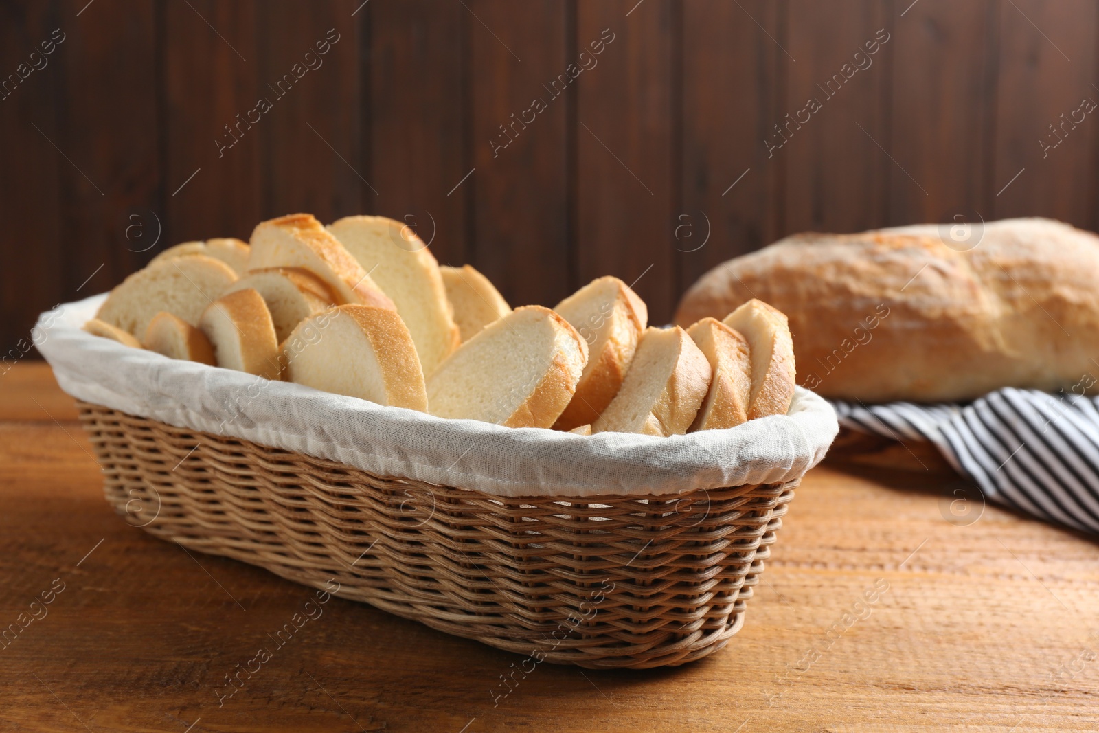 Photo of Slices of tasty fresh bread in wicker basket on wooden table