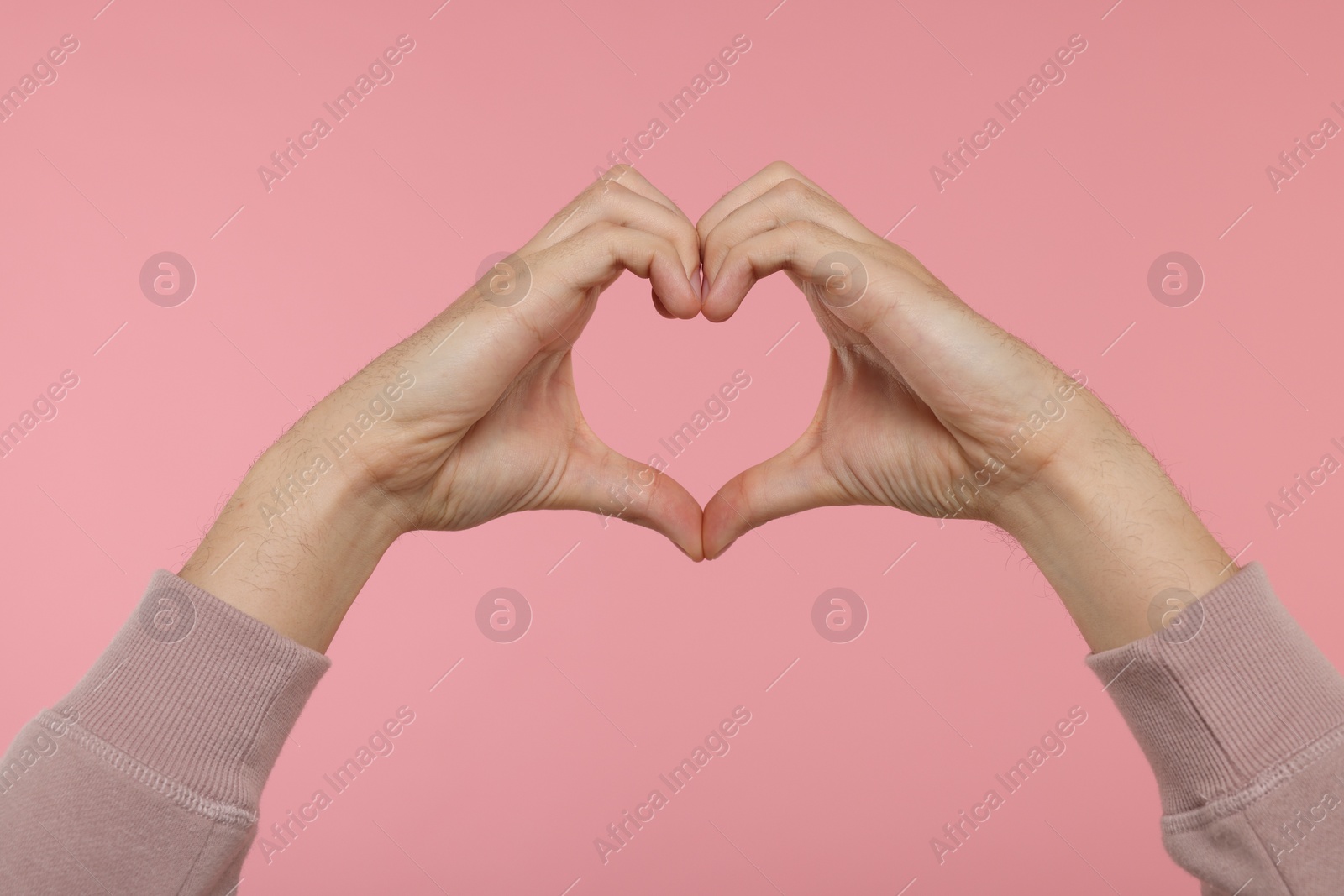 Photo of Man showing heart gesture with hands on pink background, closeup