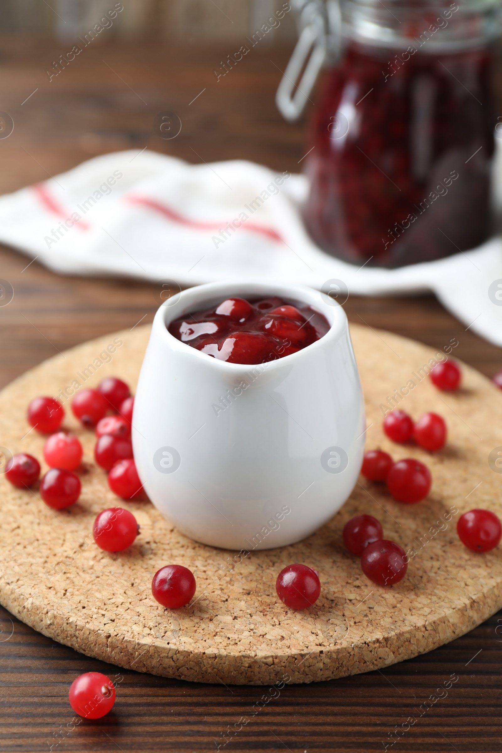 Photo of Cranberry sauce in pitcher and fresh berries on wooden table, closeup