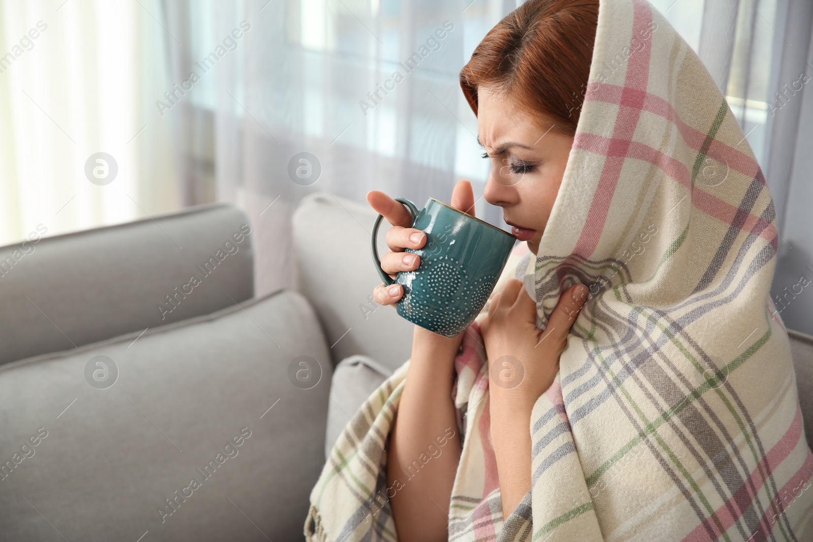 Photo of Sick woman wrapped in plaid with cup of hot drink at home. Influenza virus