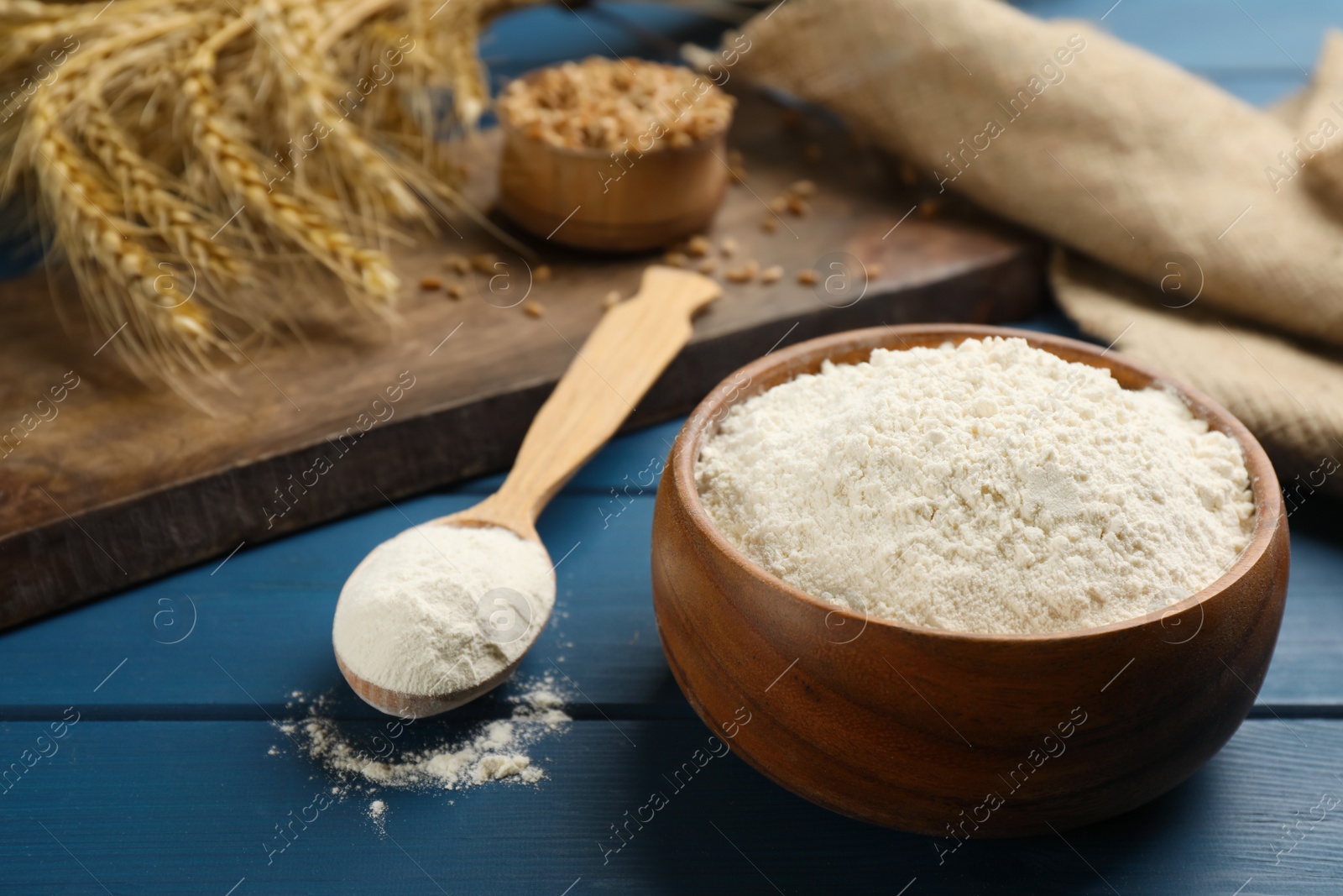 Photo of Wooden bowl and spoon with flour on blue wooden table