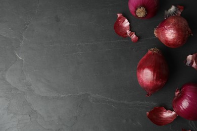 Photo of Ripe red onion bulbs on black table, flat lay. Space for text