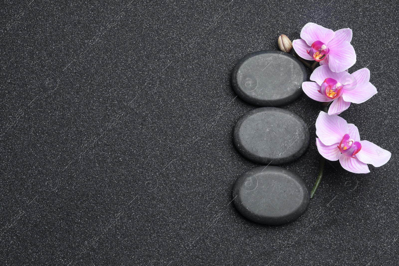 Photo of Flat lay composition with stones and orchid flowers on black sand, space for text. Zen concept