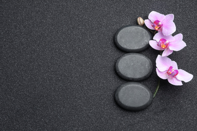 Flat lay composition with stones and orchid flowers on black sand, space for text. Zen concept