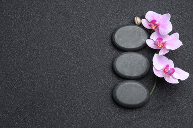 Photo of Flat lay composition with stones and orchid flowers on black sand, space for text. Zen concept