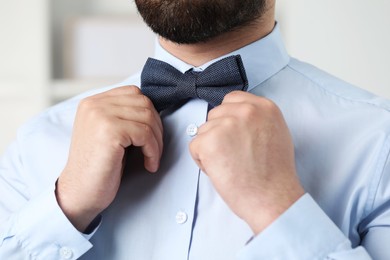 Man in shirt adjusting bow tie indoors, closeup