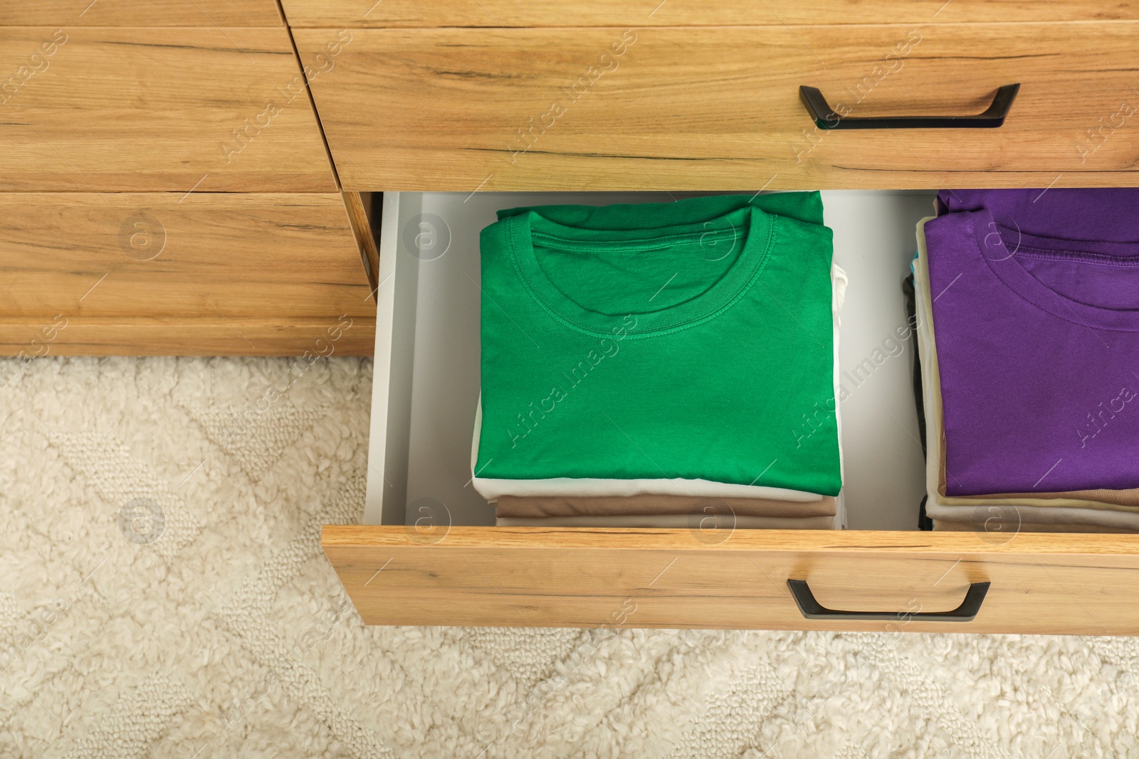 Photo of Stacks of different folded shirts in drawer indoors, top view. Organizing clothes