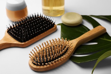 Wooden hairbrushes, cosmetic products and green leaf on white background, closeup