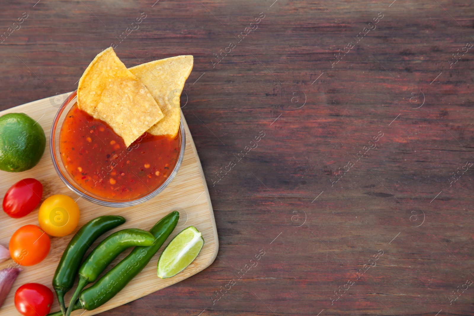 Photo of Tasty salsa sauce with tortilla chips and ingredients on wooden table, top view. Space for text